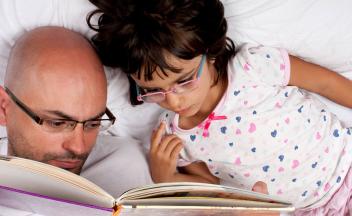 Bird's eye view of father reading picture book to daughter