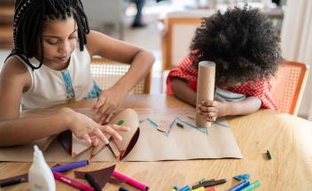 Two young kids at home creating things out of cardboard and markers